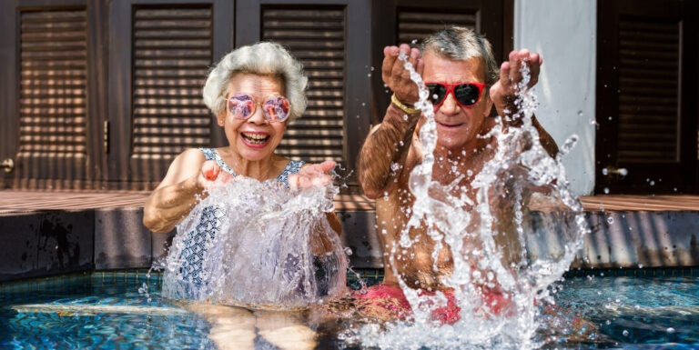 Elderly Couple Splashing Water Playfully by Pool at Independent Living Facility